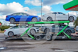 The car carrier transports new cars. A trailer for transporting cars is at a gas station. The concept of road transportation