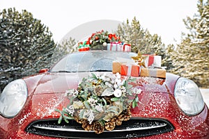 Car with Christmas wreath, tree and gifts in winter forest