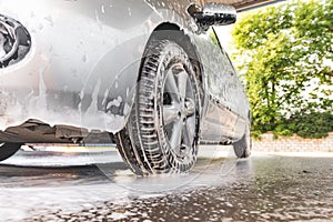 The car is covered with foam at a self-service car wash. Close-up of front bumper and wheel