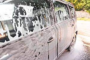 The car is covered with foam at a self-service car wash. Close-up of side windows