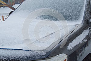 The car is covered with snow on a winter day, front window windshield and hood view on a snowy background