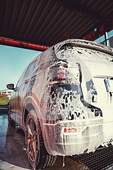 A car covered in soapy suds at an outdoor self-service car wash station