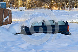 Car covered with thick layer of snow at night. Automobile after snowstorm parked on the street side