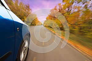 A car on curvy autumn forest road, with motion blur from its speed
