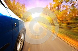 A car on curvy autumn forest road, with motion blur from its speed