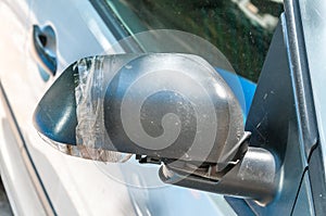 Car with damaged and broken side rear mirror glued with duct tape close up selective focus