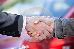 Car dealer and female client shaking hands at dealership