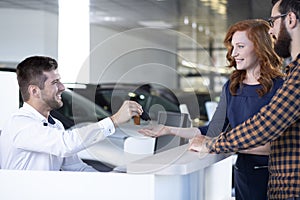 Car dealer giving car keys to a happy couple in a car showroom