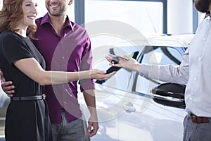 Car dealer giving keys to happy woman and smiling man in a dealing salon