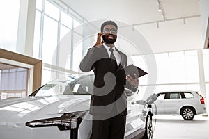 Car dealer holding clipboard in automobile showroom.