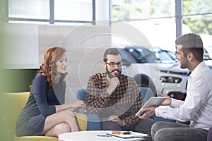 Car dealer showing an offer to his happy clients in a car showroom