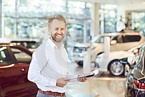 A car dealer smiling standing in a showroom.