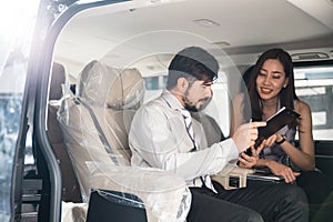 Car Dealership. The Asian Salesman woman checking the list with the middle east customer inside the new car with plastic wrapped