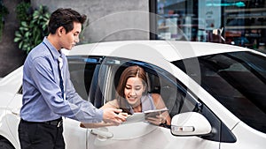 Car Dealership. The Asian woman receiving a car key with a smile form the salesman before hand over. Auto Leasing Business.