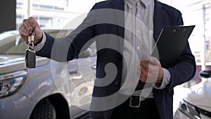 Car dealership, car manager male holds in hands keys to new auto for sale in showroom