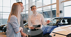 Car Dealership. Cheerful Elegant Manager Guy Showing Automobile To Customers