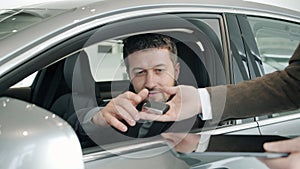 Car dealership client getting key fob from sales manager sitting inside new car