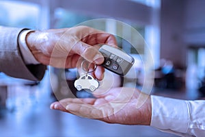 At a car dealership, a sales manager hands over a car key to a buyer.