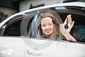 Car dealership. The woman showing a car key in her palm with smiling while sitting inside the car