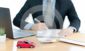 A car on desk envelope with man signing purchase documents in background. while hand complete the insurance policy, rental
