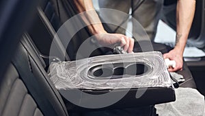 Car detailing concept, young man cleaning vehicle seats with a rag and a brush in car studio, car care