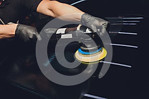 Car detailing - Hands with orbital polisher in auto repair shop. Selective focus.