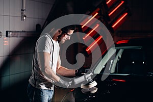 Car detailing - man with orbital polisher in auto repair shop. Selective focus.