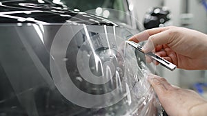 Car detailing. Male specialist applying window tinting film on the car and cuts off excess part with a knife. The master