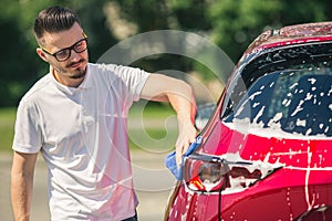 Car detailing - the man holds the microfiber in hand and polishes the car. Man worker washing car`s alloy wheels on a car wash.