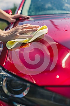 Car detailing - the man holds the microfiber in hand and polishes the car. Man worker washing car`s alloy wheels on a car wash.