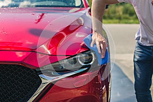 Car detailing - the man holds the microfiber in hand and polishes the car. Man worker washing car`s alloy wheels on a car wash.