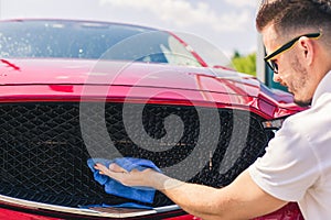 Car detailing - the man holds the microfiber in hand and polishes the car. Man worker washing car`s alloy wheels on a car wash.