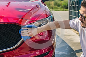 Car detailing - the man holds the microfiber in hand and polishes the car. Man worker washing car`s alloy wheels on a car wash.