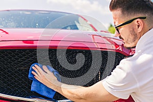 Car detailing - the man holds the microfiber in hand and polishes the car. Man worker washing car`s alloy wheels on a car wash.