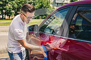 Car detailing - the man holds the microfiber in hand and polishes the car. Man worker washing car`s alloy wheels on a car wash.