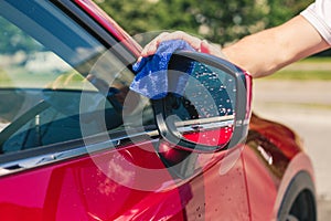 Car detailing - the man holds the microfiber in hand and polishes the car. Man worker washing car`s alloy wheels on a car wash.