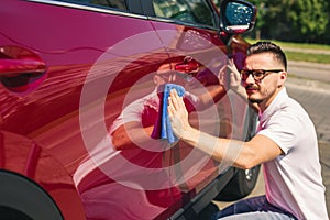 Car detailing - the man holds the microfiber in hand and polishes the car. Man worker washing car`s alloy wheels on a car wash.