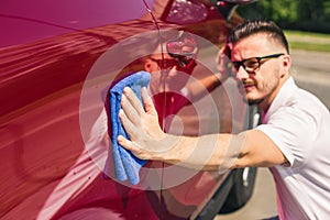 Car detailing - the man holds the microfiber in hand and polishes the car. Man worker washing car`s alloy wheels on a car wash.