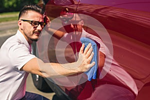 Car detailing - the man holds the microfiber in hand and polishes the car. Man worker washing car`s alloy wheels on a car wash.