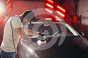 Car detailing - man with orbital polisher in auto repair shop. Selective focus.