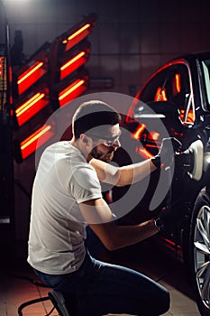 Car detailing - man with orbital polisher in auto repair shop. Selective focus.