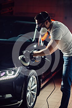 Car detailing - man with orbital polisher in auto repair shop. Selective focus.