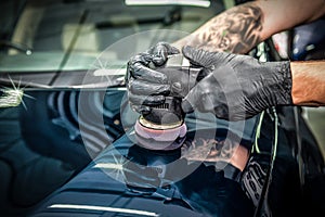 Car detailing and polishing concept. Hands of professional car service male worker, with orbital polisher, polishing yellow luxury