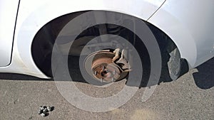 Car disc brake of white vehicle raised on jack. Tire and wheel replacement. Auto repair shop. Dirty surface of wheel arches.