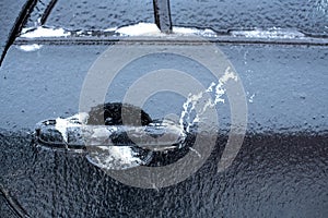 Car door opener handle with ice on top at shallow depth of field