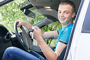 Car driver. Caucasian teen boy showing car key in the new car.