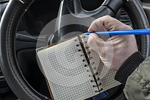 Car driver hand holds a pen and writes notes in a notebook