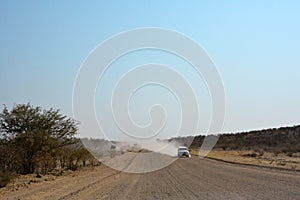 A car drives along a wide dirt road in the desert in perspective. A journey through arid lands