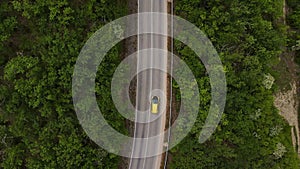 A car drives down a paved road in a mountainous area that cuts through a forest