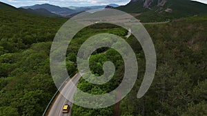 A car drives down a paved road in a mountainous area that cuts through a forest